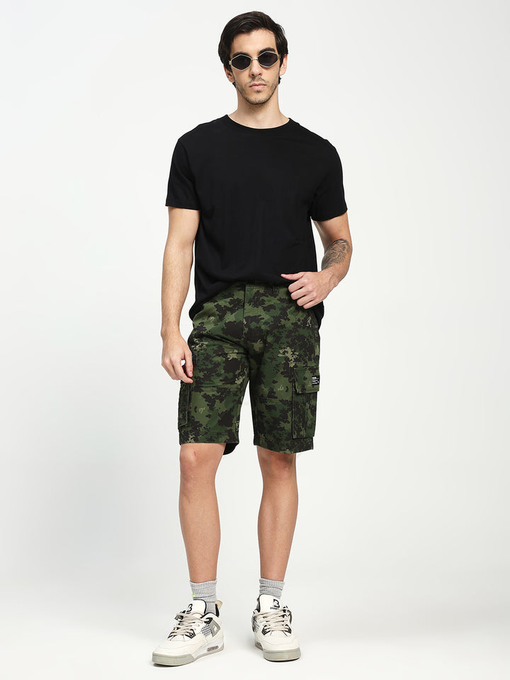 Man wearing a black t-shirt, green camouflage shorts, and white sneakers on a white background