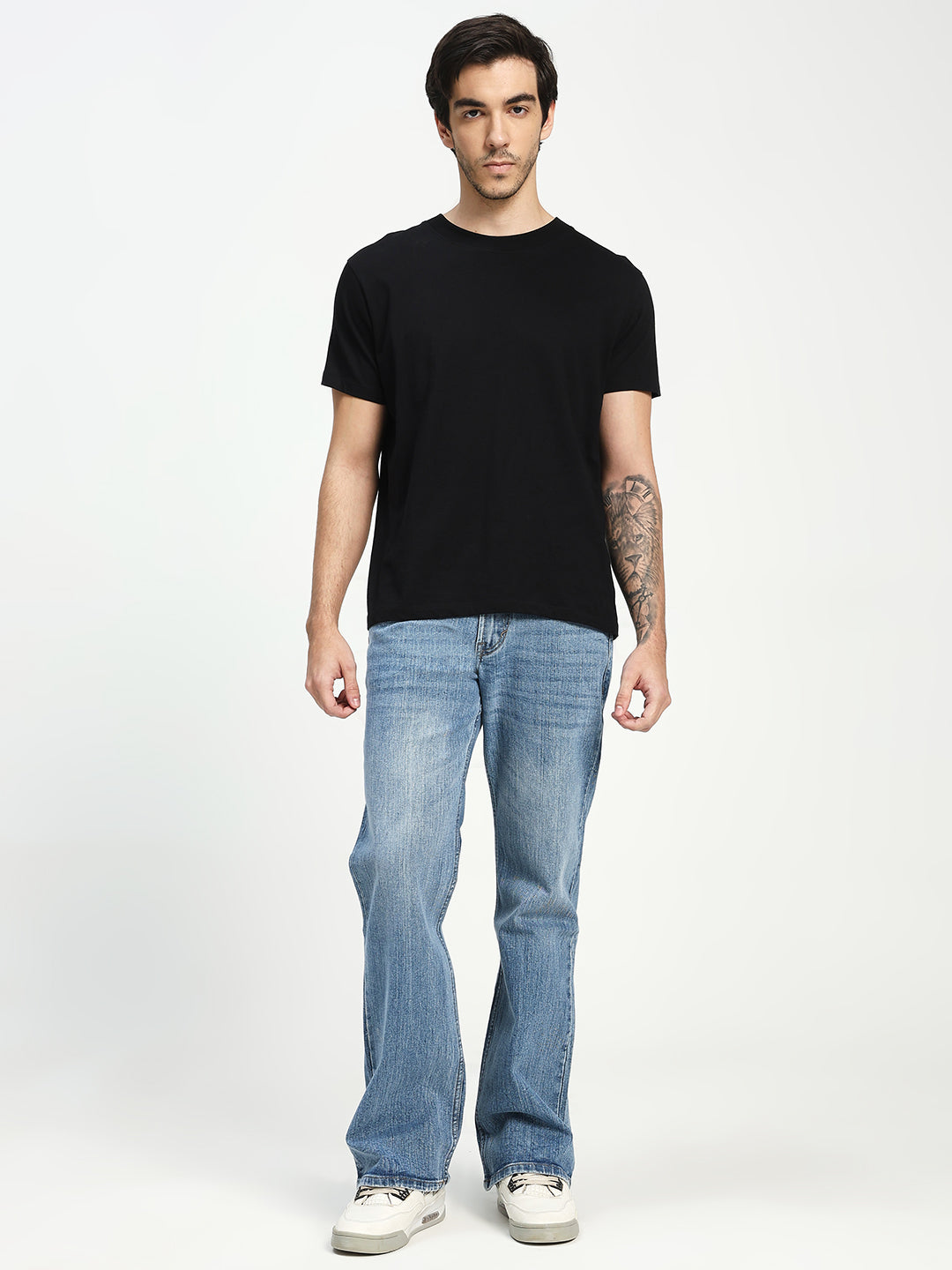 Man wearing a black t-shirt and blue bootcut jeans on a white background