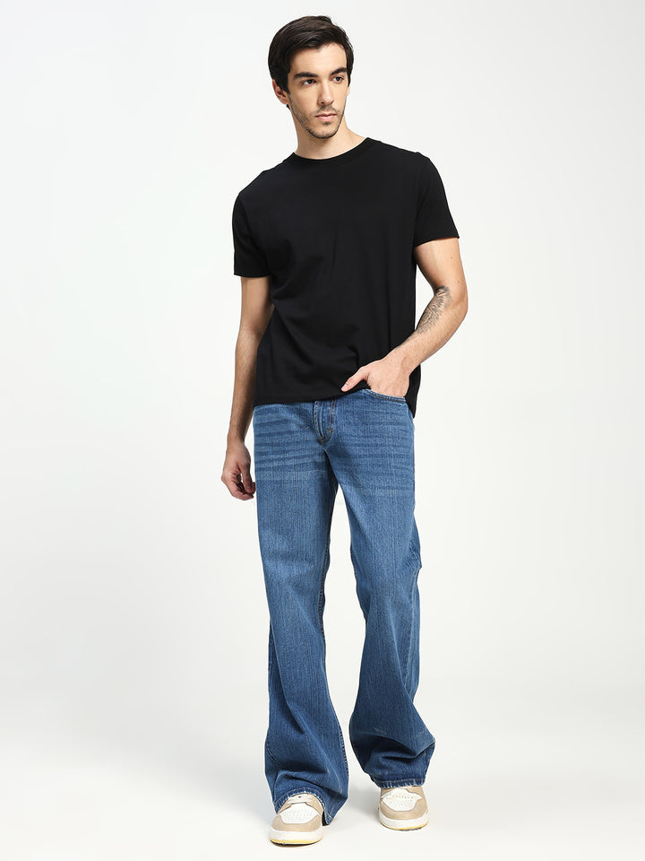Man wearing a black t-shirt and blue bell bottom jeans on a white background