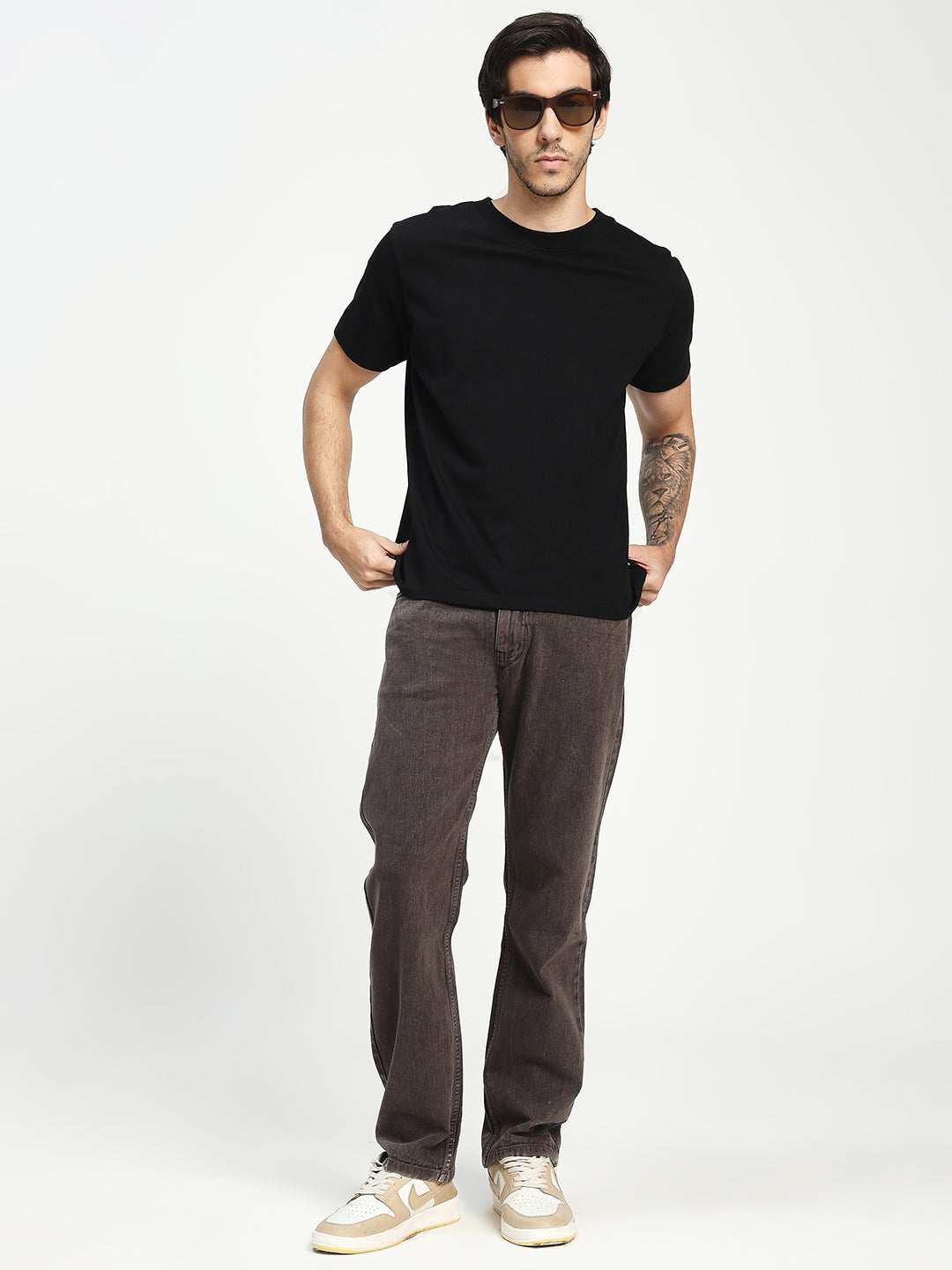 Man wearing a black t-shirt and dARK ecru brown pants on a white background