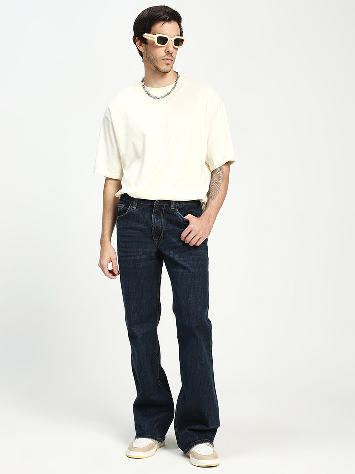 Man wearing a white t-shirt, bell bottom dark jeans, and sunglasses on a white background