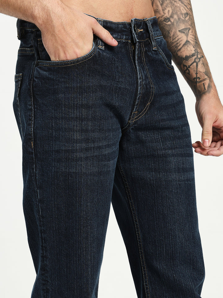 man wearing dark blue bell bottom jeans with a tattooed arm on a white background