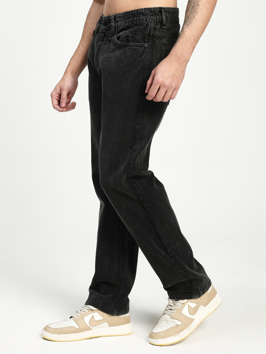 man wearing charcoal acru jeans and beige sneakers on a white background