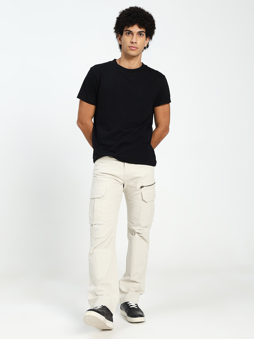 man wearing a black t-shirt and cream cargo pants on a white background
