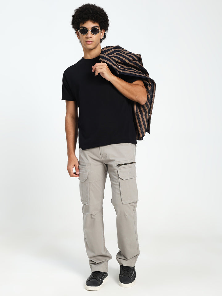 Man wearing a black t-shirt, grey cargo pants, and sunglasses, holding a patterned bag on a white background