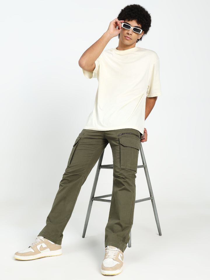 man wearing a white t-shirt and olive green cargo pants sitting on a stool against a white background
