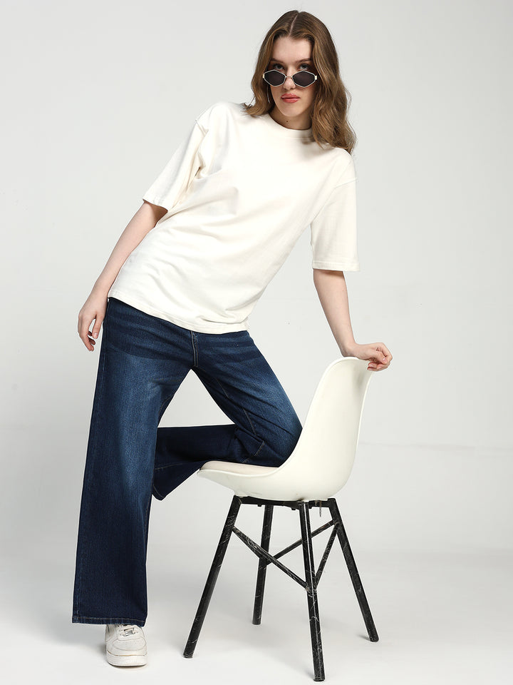 Woman sitting on a white chair wearing a white t-shirt and blue jeans against a plain background