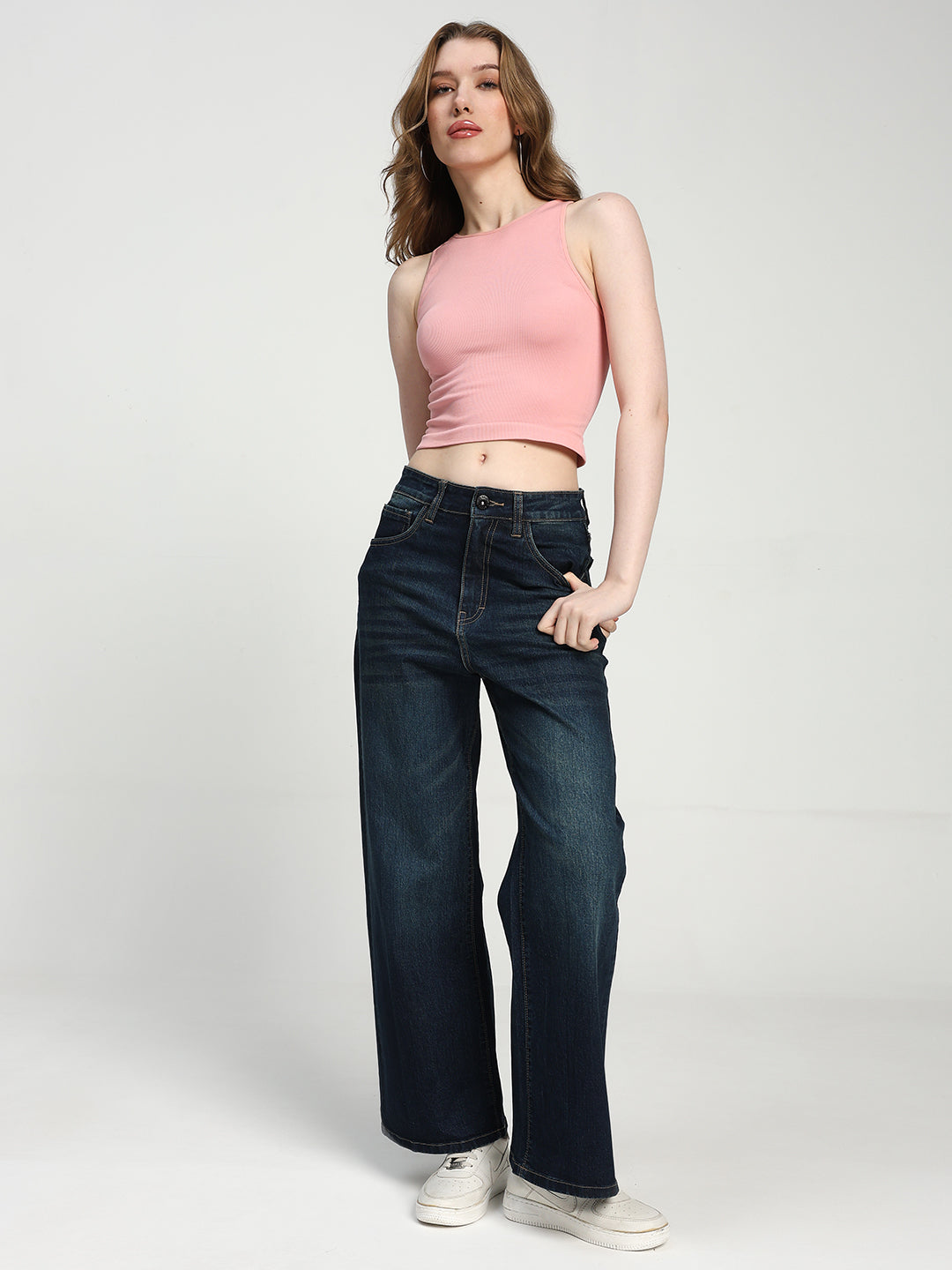 Woman wearing a pink sleeveless top and dark blue jeans on a white background