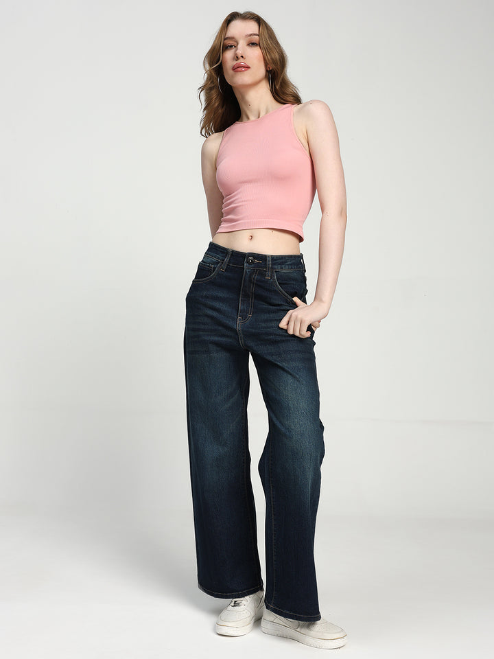Woman wearing a pink sleeveless top and dark blue jeans on a white background