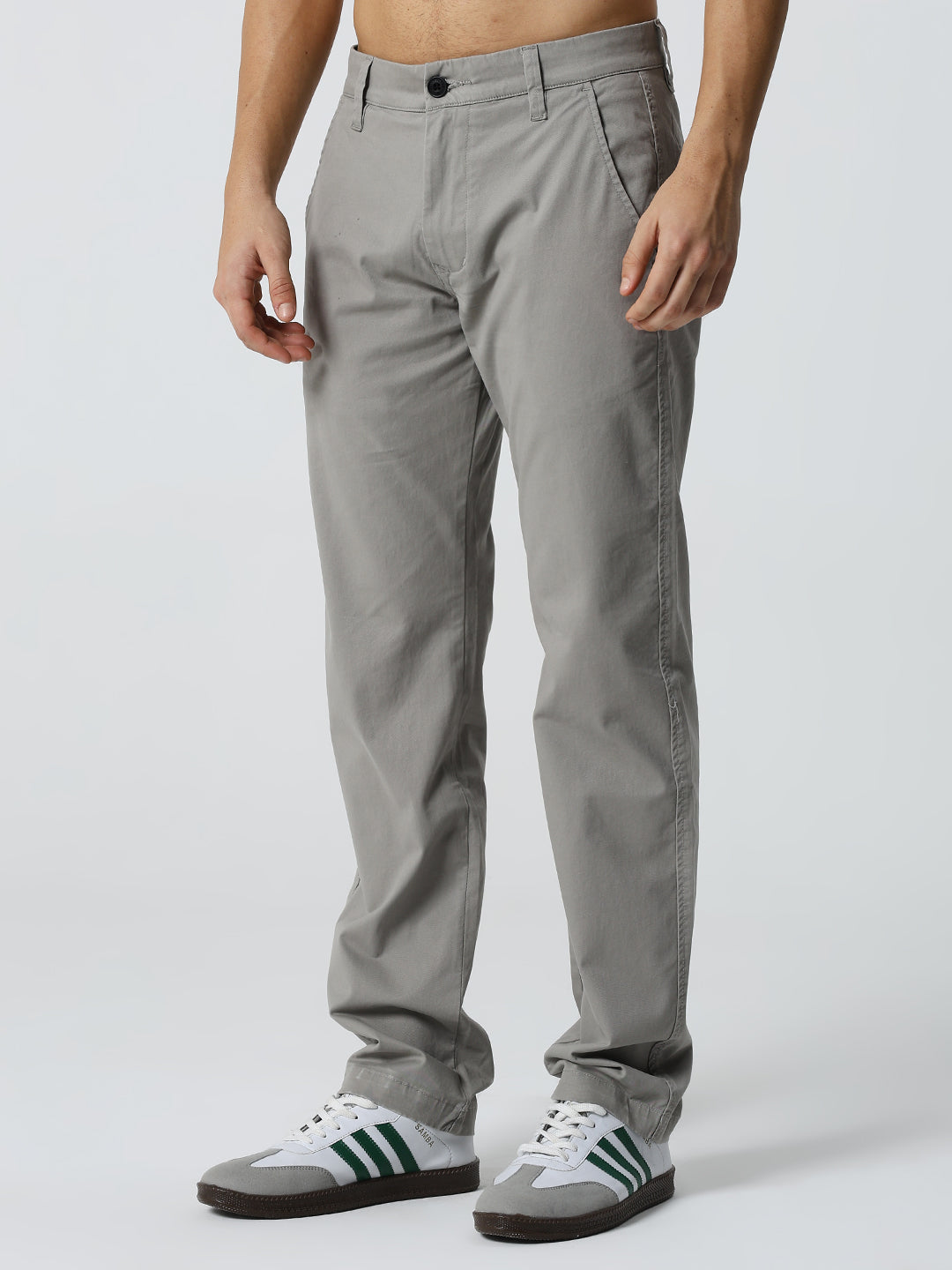 man wearing gray pants and white sneakers with green stripes on a light gray background