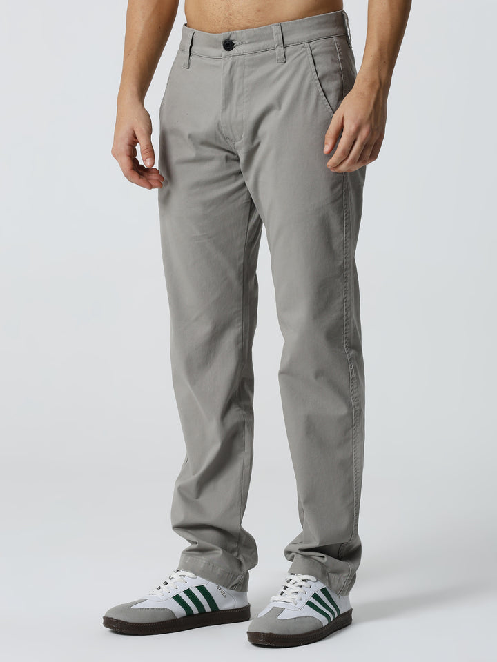 man wearing gray pants and white sneakers with green stripes on a light gray background