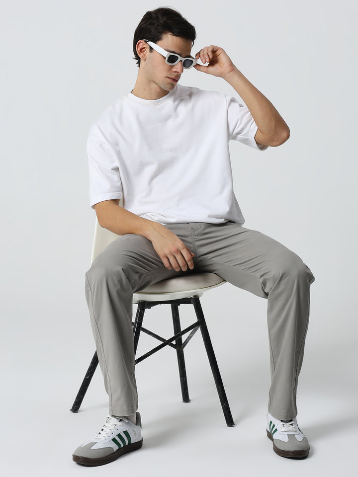 man sitting on a chair wearing a white t-shirt, gray pants, and shoes against a plain background.