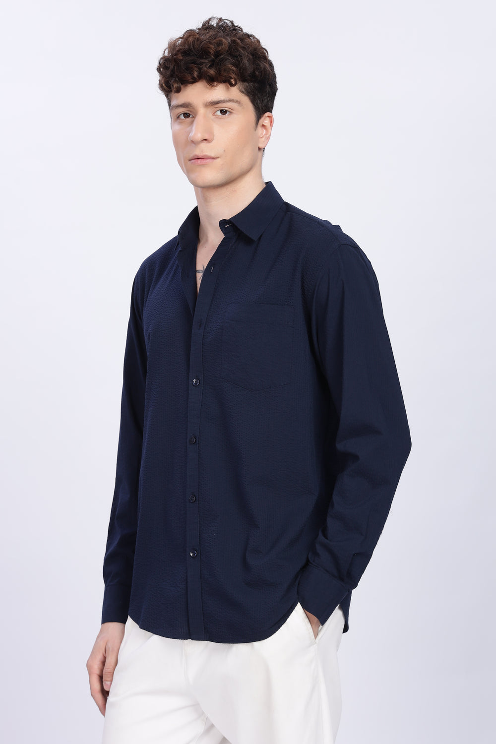 Man wearing a navy blue shirt and white pants on a light gray background