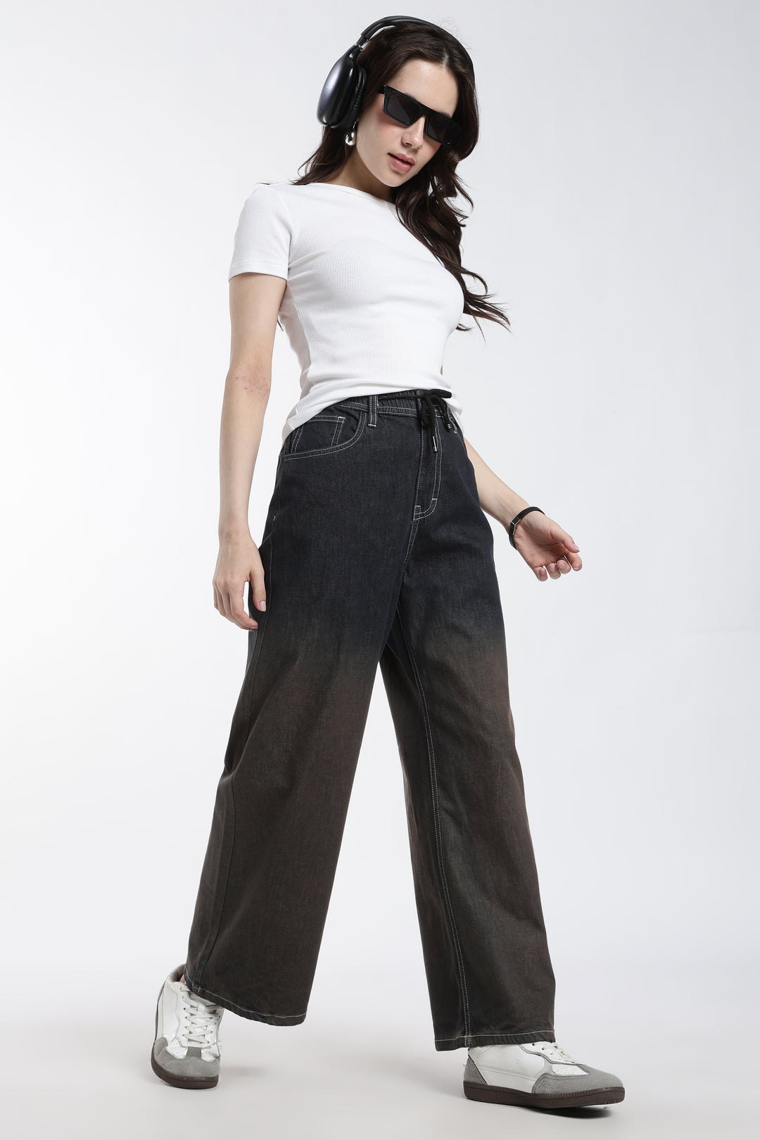 Woman wearing a white t-shirt, dark vintage wash wide-leg denim jogger, and headphones on a white background