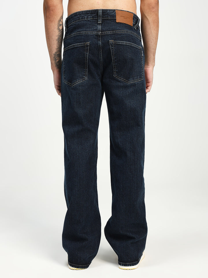 Dark blue bell bottom jeans worn by a man on a white background