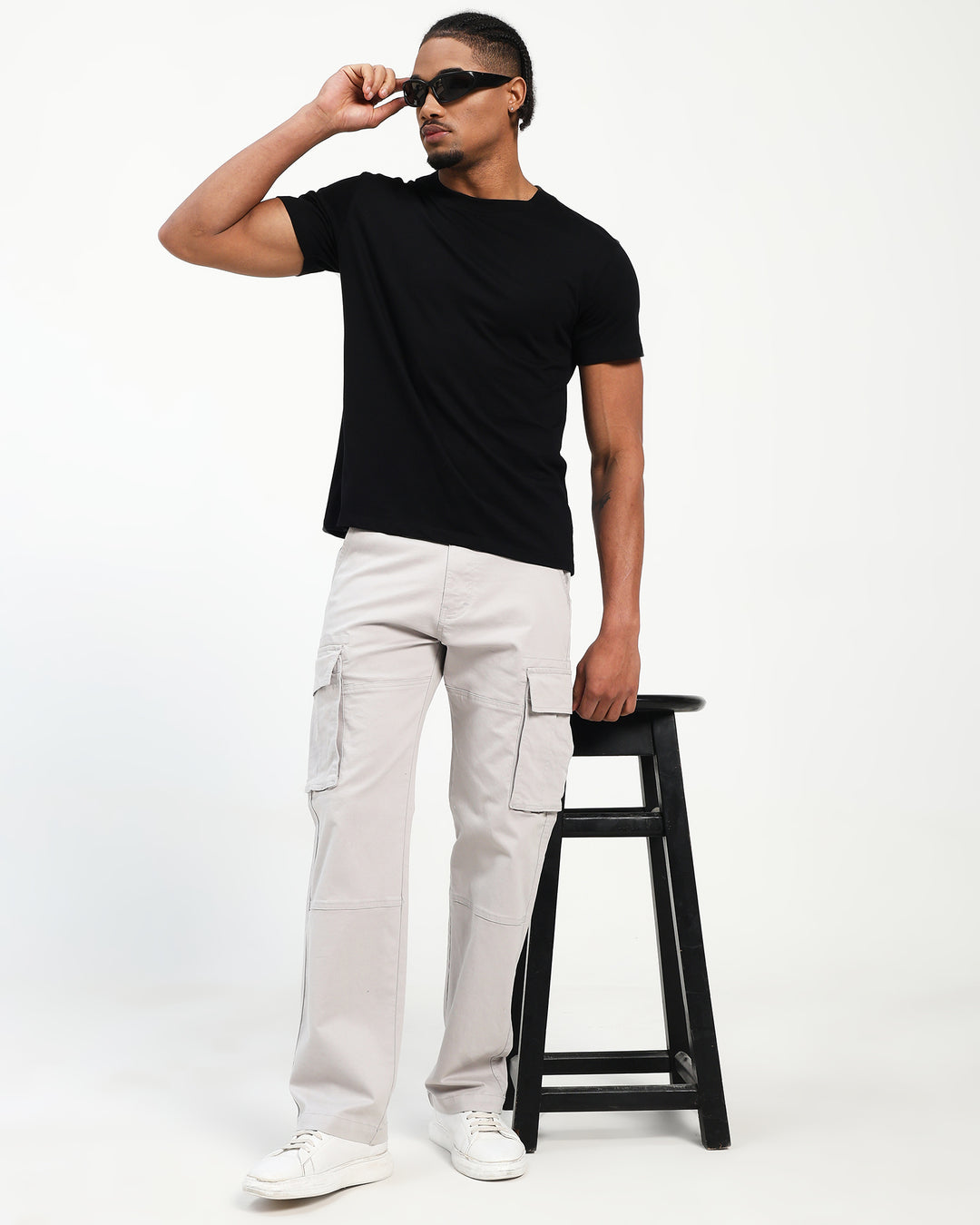 man wearing a black t-shirt and white pants standing on a stool against a white background