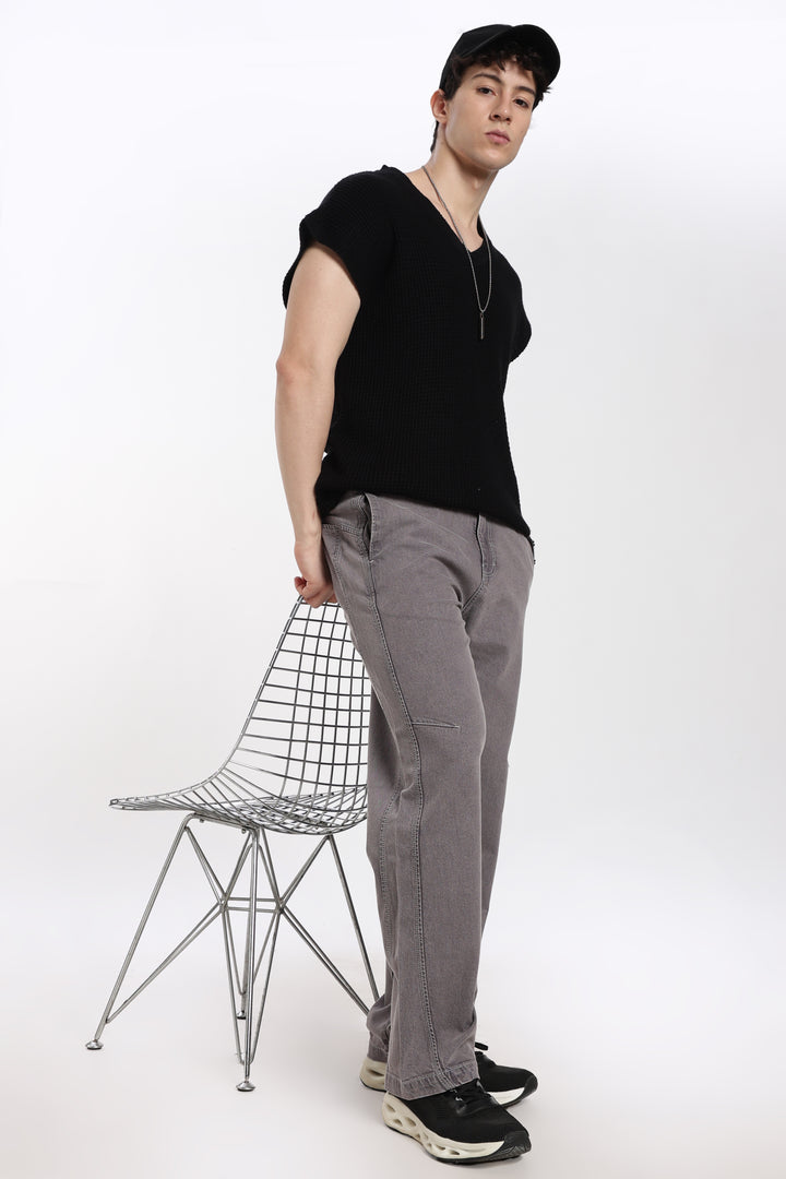 man wearing a black sleeveless t-shirt and gray jogger standing next to a wire chair on a white background