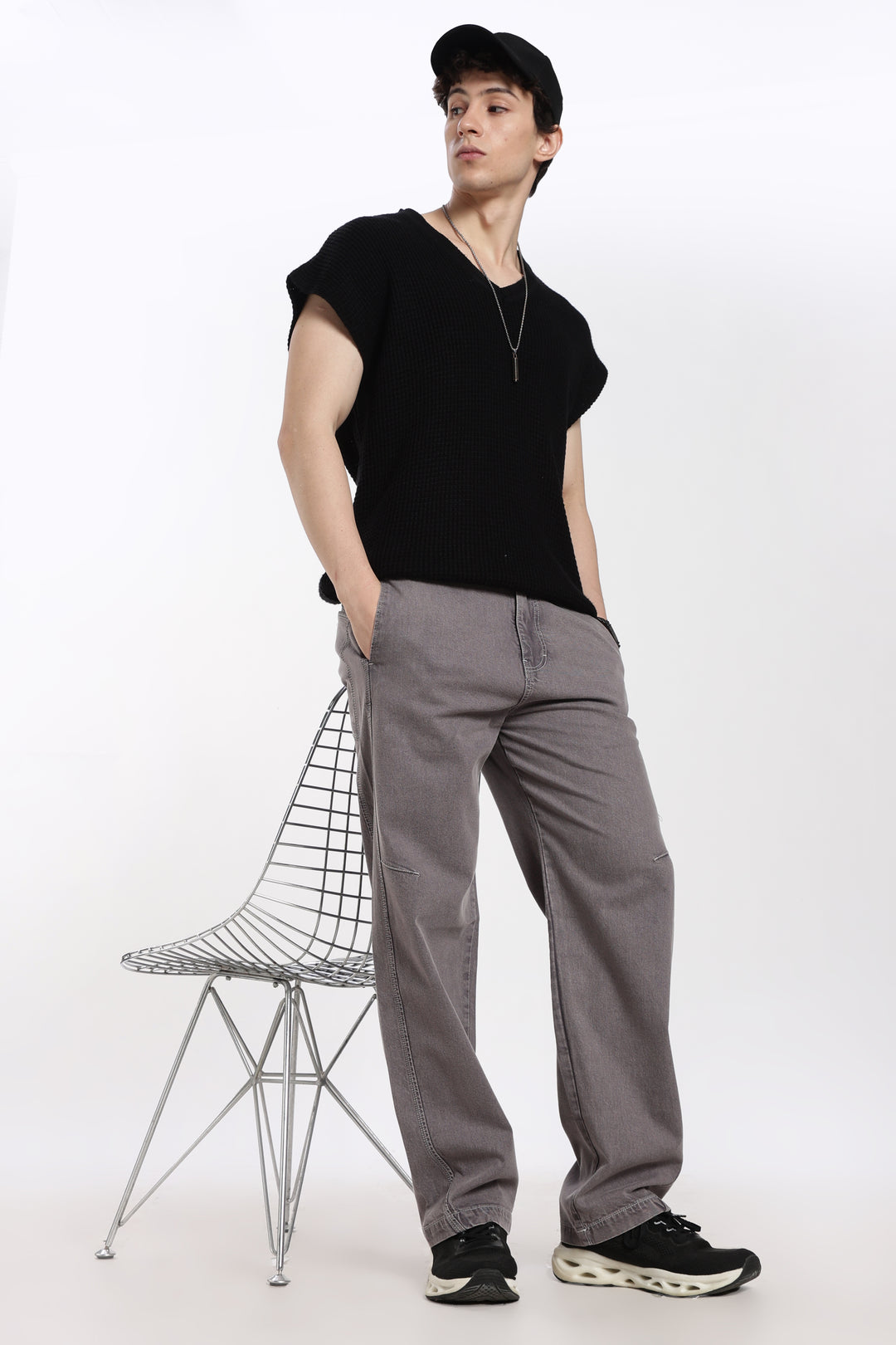 man wearing a black t-shirt and gray jogger standing next to a wire chair on a white background