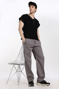 man wearing a black t-shirt and gray jogger standing next to a wire chair on a white background
