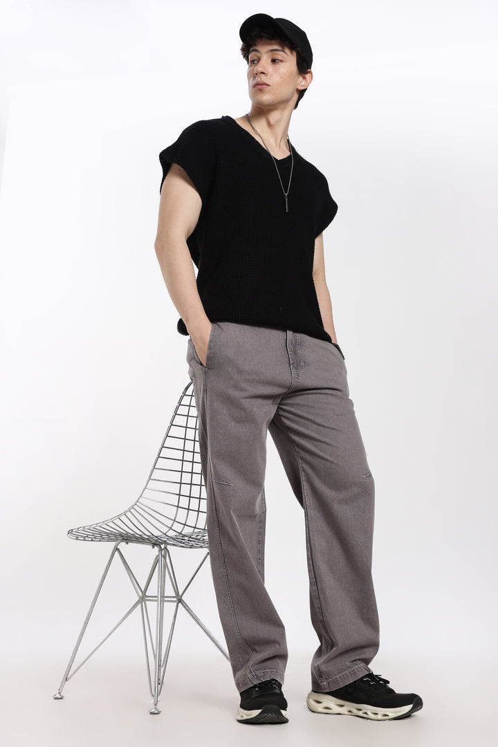 man wearing a black t-shirt and gray jogger standing next to a wire chair on a white background