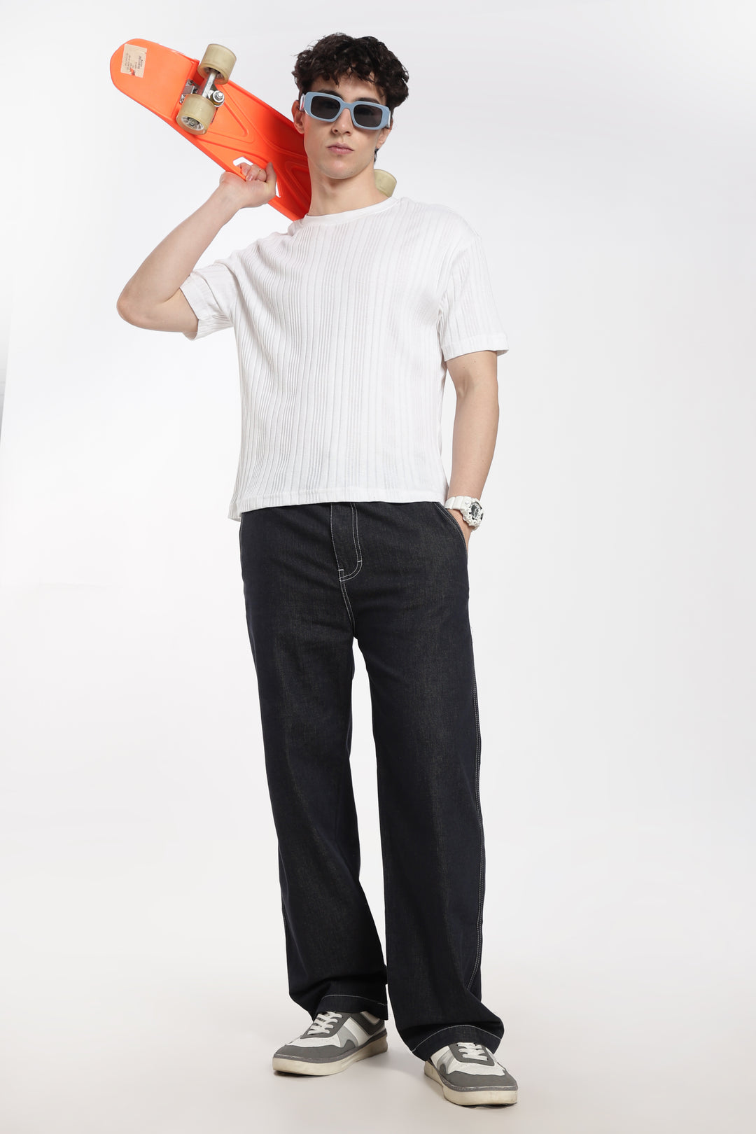 man holding an orange skateboard wearing a white t-shirt and dark wash denim jogger pants on a white background