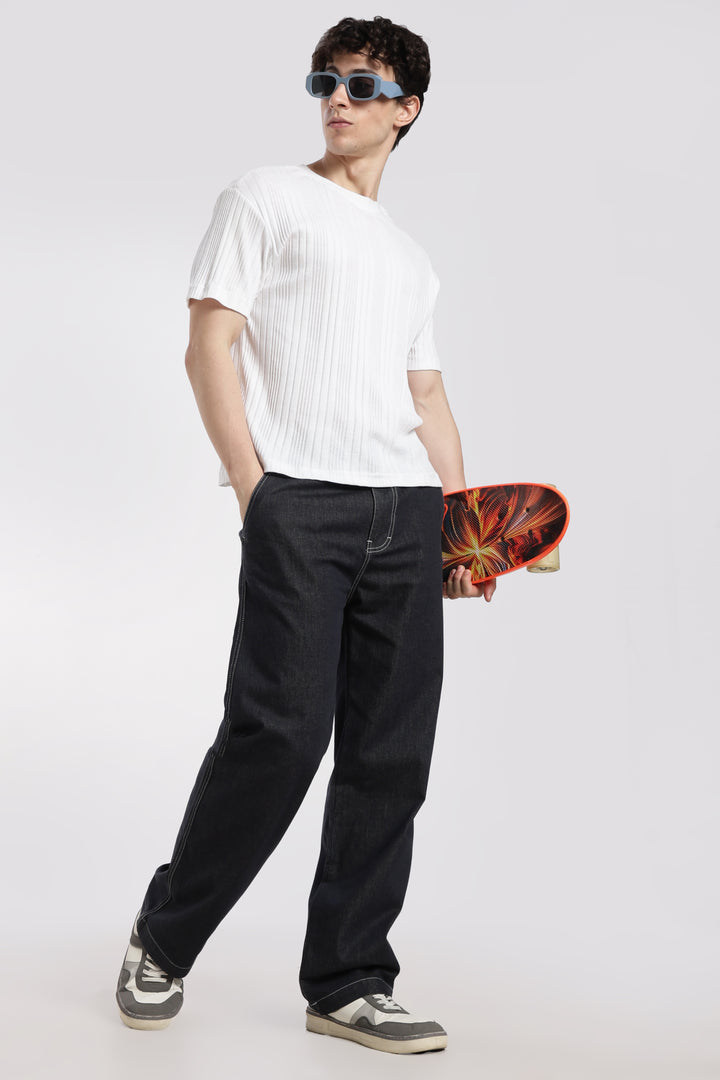 man wearing a white t-shirt, dark wash denim jogger pants, and sunglasses, holding a colorful skateboard.