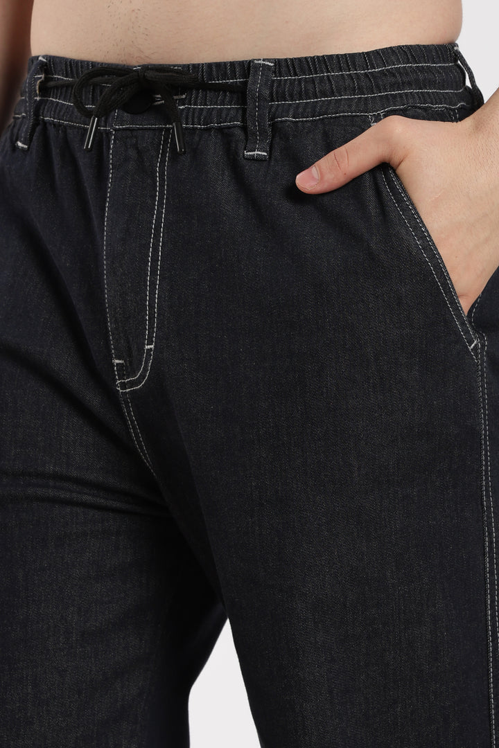 dark wash denim jogger pants with a belt being worn, on a plain background