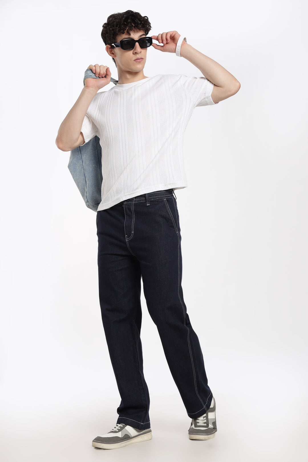 man wearing a white t-shirt, navy blue denim jogger pant, and sunglasses on a white background