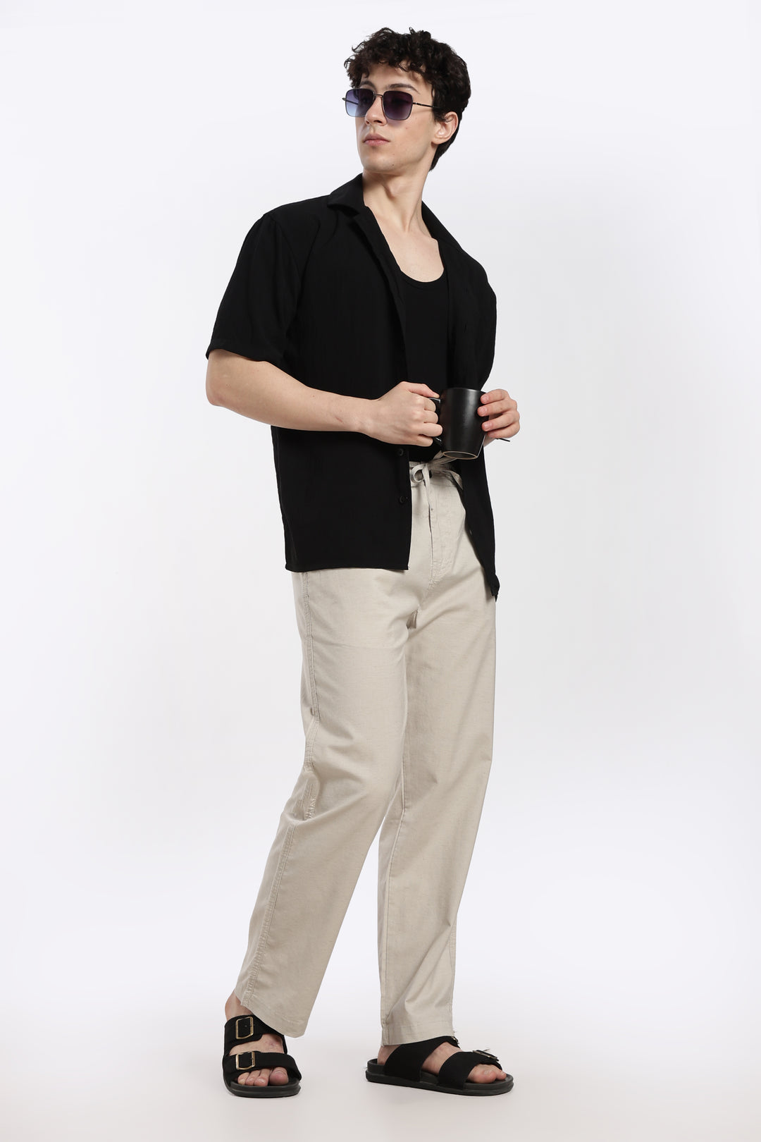 man wearing a black shirt, desert sand pants, and sandals on a white background