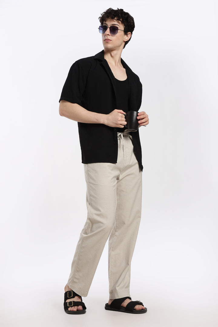 man wearing a black shirt, desert sand pants, and sandals on a white background