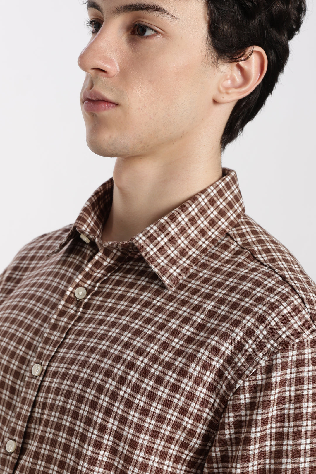man wearing a brown and white checkered half sleeve shirt against a plain background