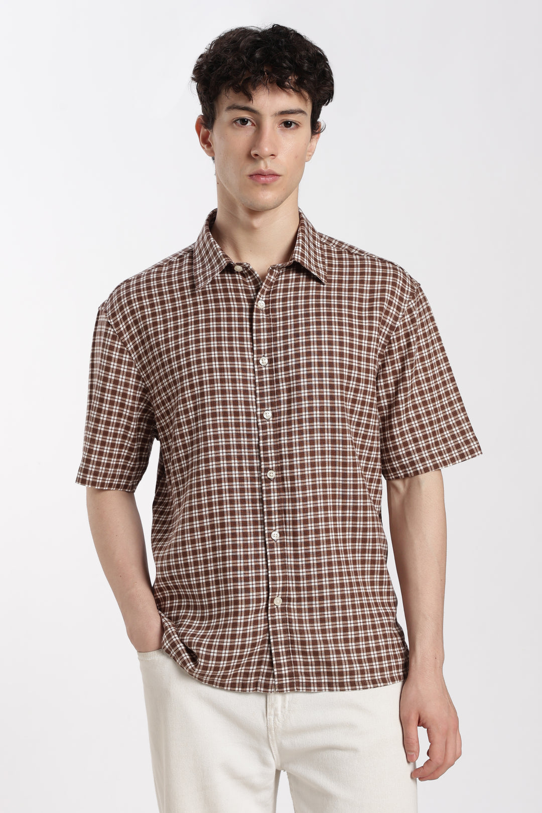 Man wearing a brown checkered half sleeve shirt and white pants on a white background