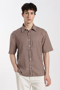 Man wearing a brown checkered half sleeve shirt and white pants on a white background