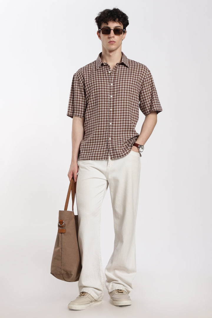 Man wearing a checkered half sleeve shirt and white pants holding a brown bag on a white background