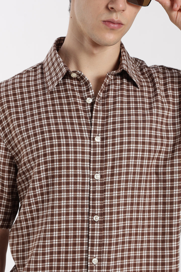 Brown checkered half sleeve shirt worn by a man on a plain background