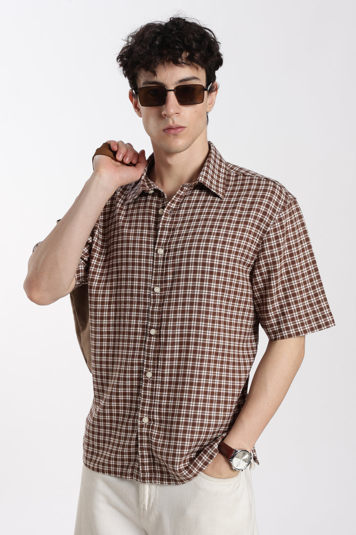 Man wearing a brown checkered half sleeve shirt and sunglasses on a white background