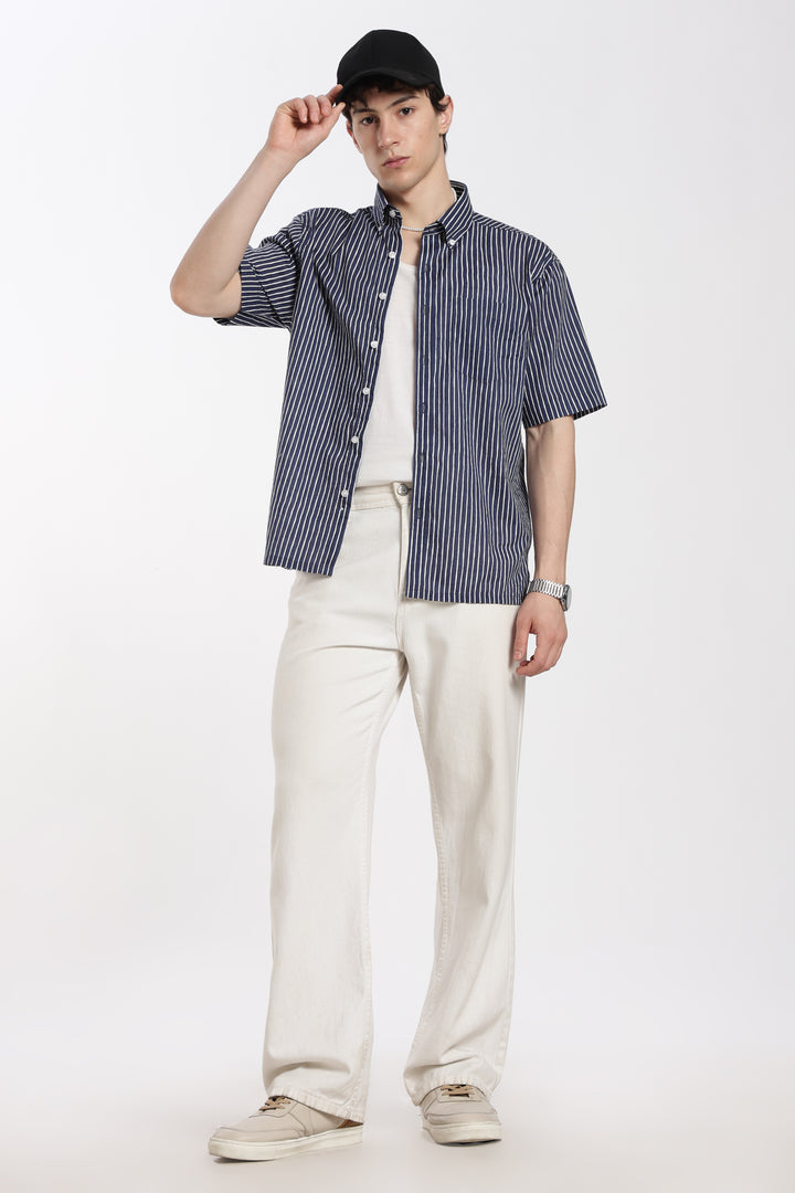 man wearing a blue striped half sleeve shirt, white pants, and a black cap on a white background
