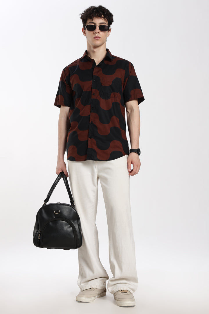 Man wearing a patterned half sleeve shirt and white pants, holding a black bag on a white background