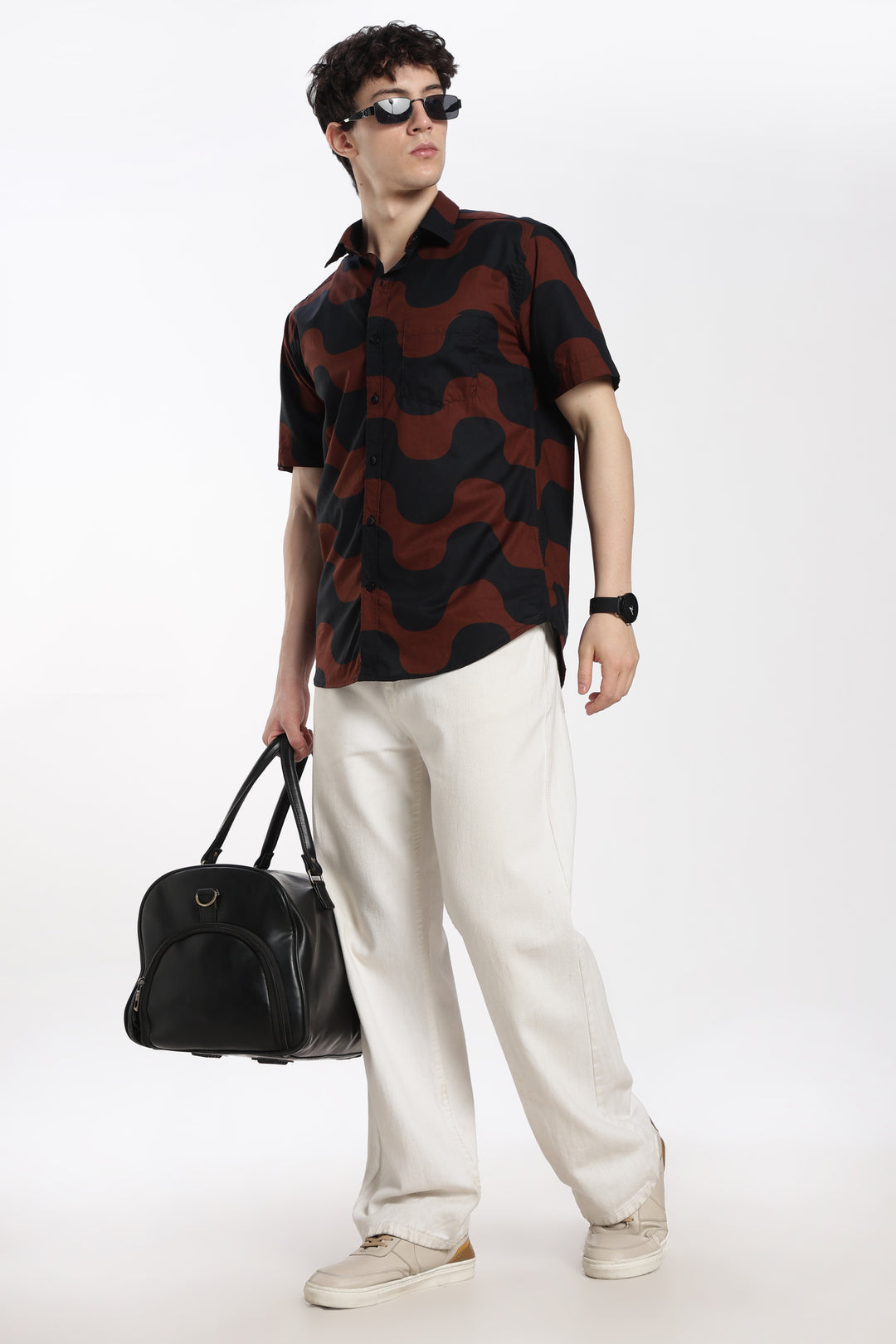 Man wearing a patterned half sleeve shirt and white pants, holding a black bag on a white background