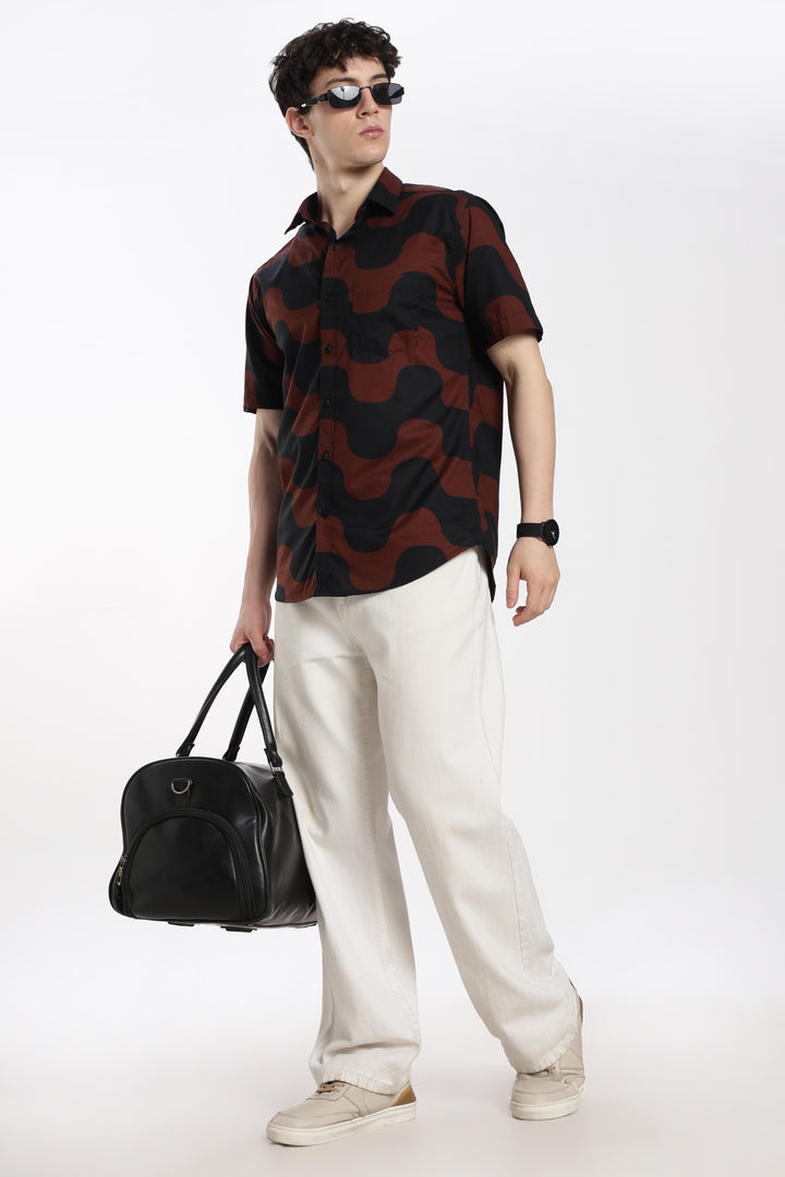 Man wearing a patterned half sleeve shirt and white pants, holding a black bag on a white background