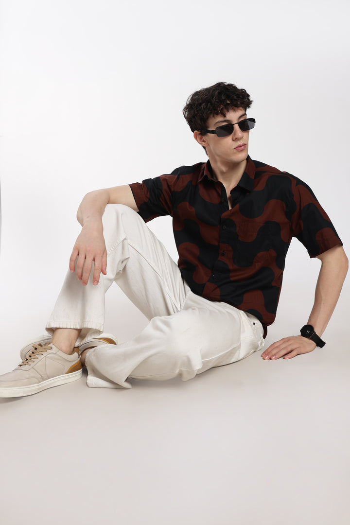 man wearing a patterned half sleeve shirt and white pants sitting on a white background