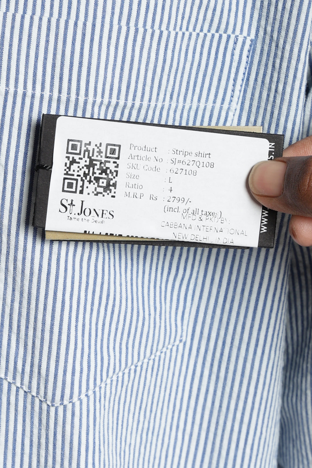 Close-up of a linen shirt label with a QR code and text, held by a hand against a blue and white striped shirt background.