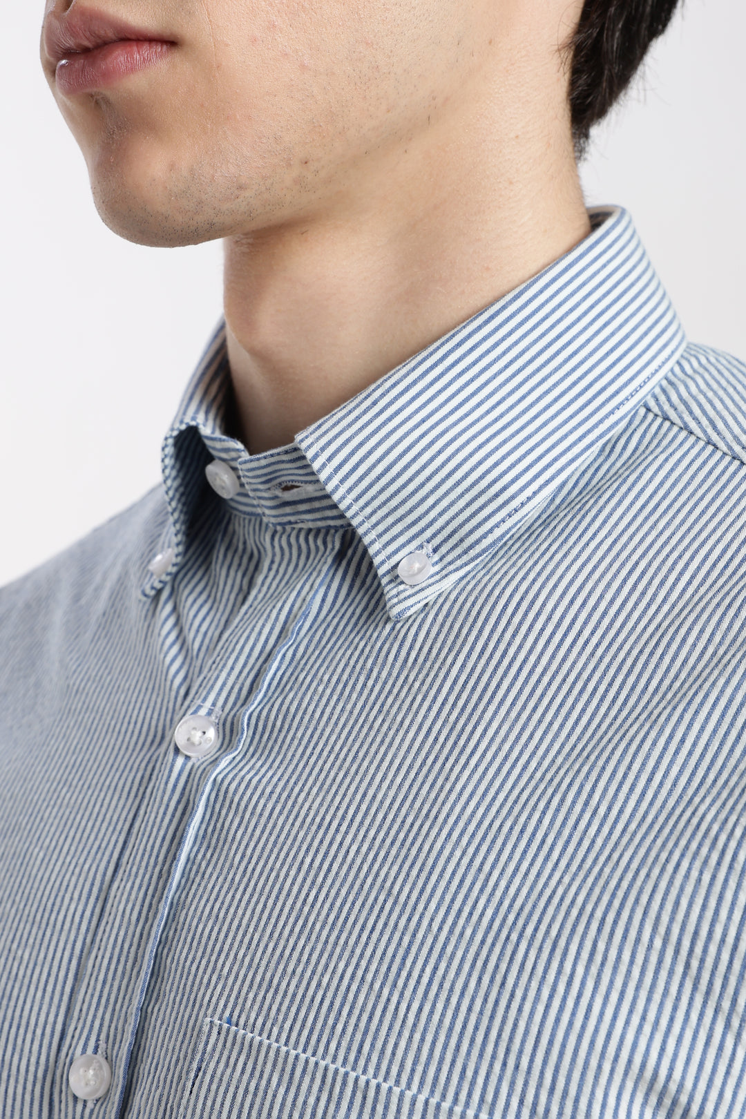 Close-up of a person wearing a blue and white striped linen shirt with a plain background