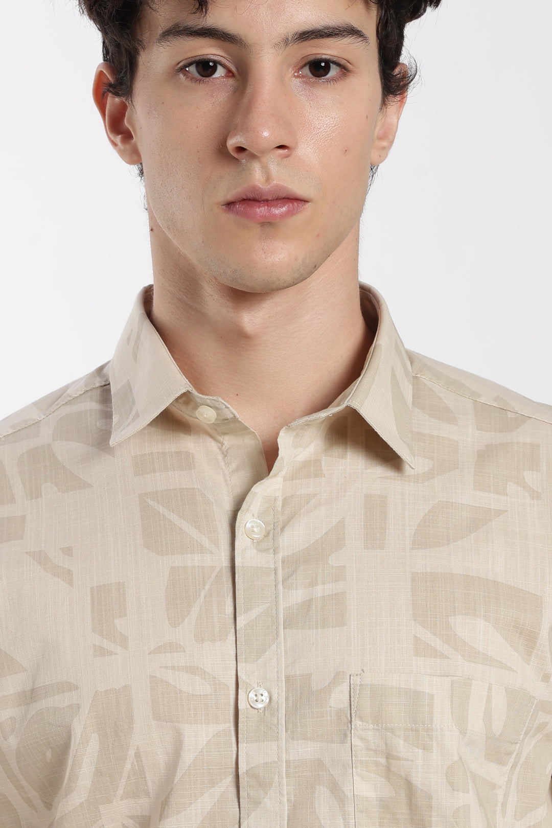 Man wearing a beige patterned half sleeve shirt against a white background