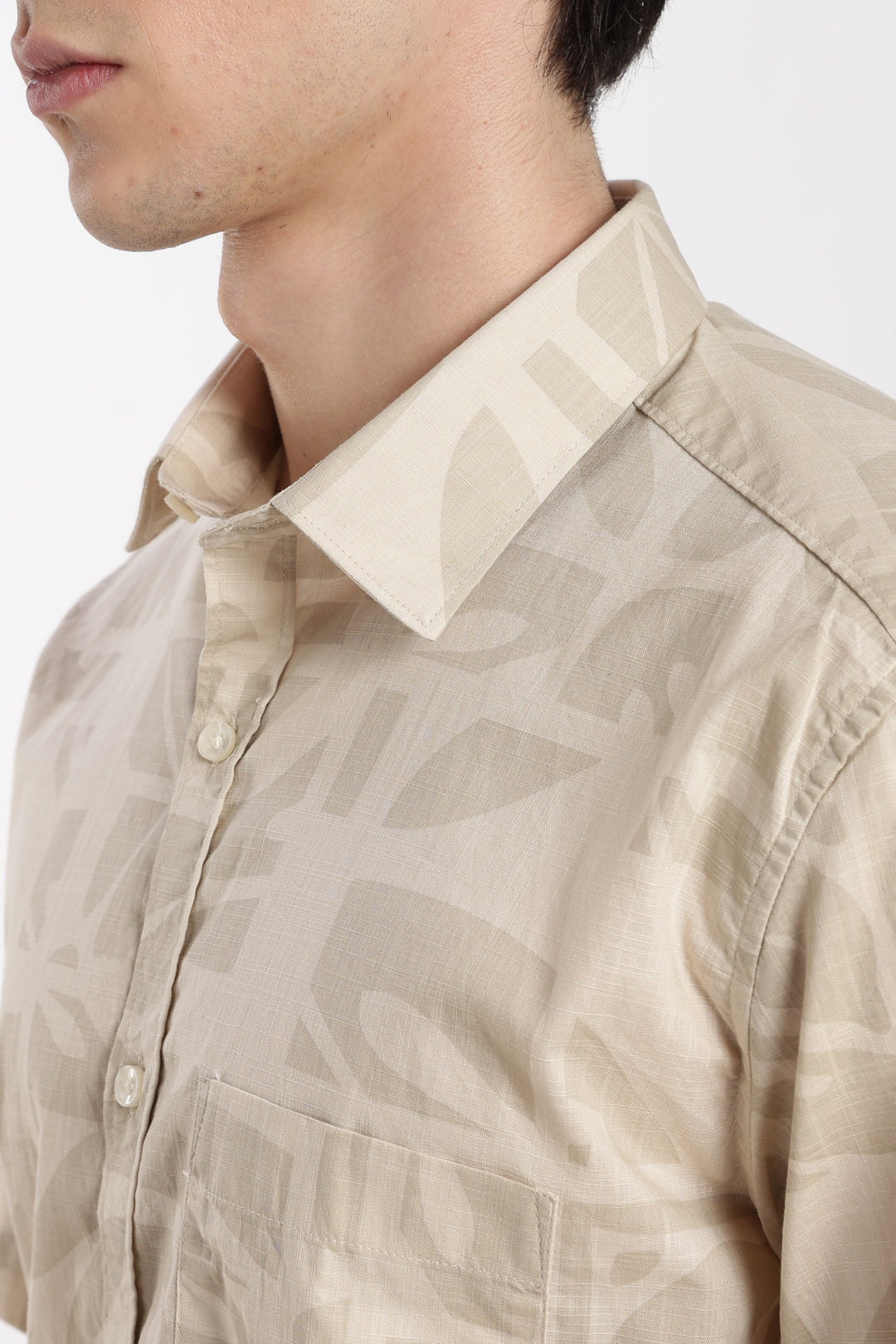 Close-up of a beige patterned half sleeve shirt with a white collar on a plain background