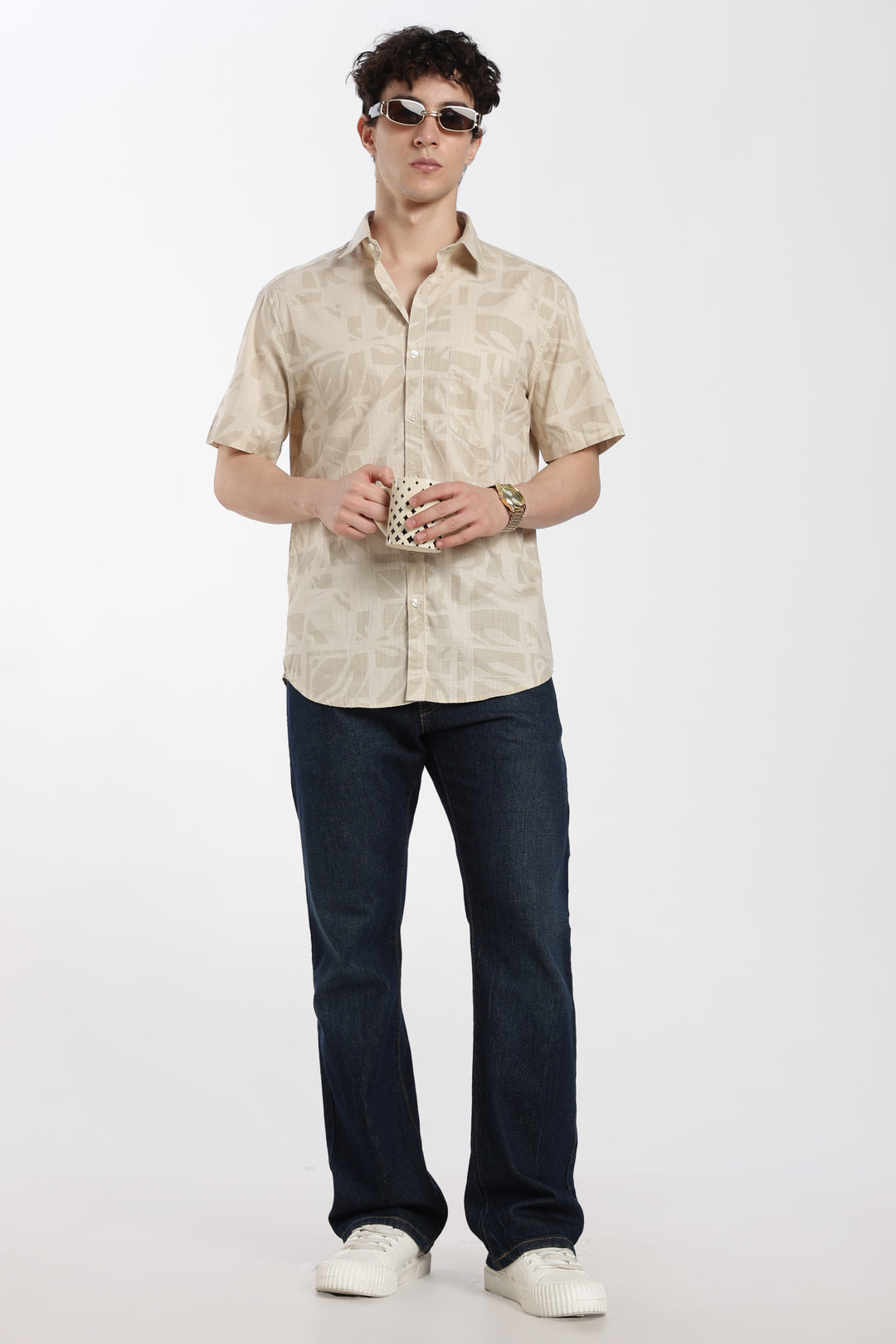 Man wearing a beige half sleeve shirt and dark jeans on a white background