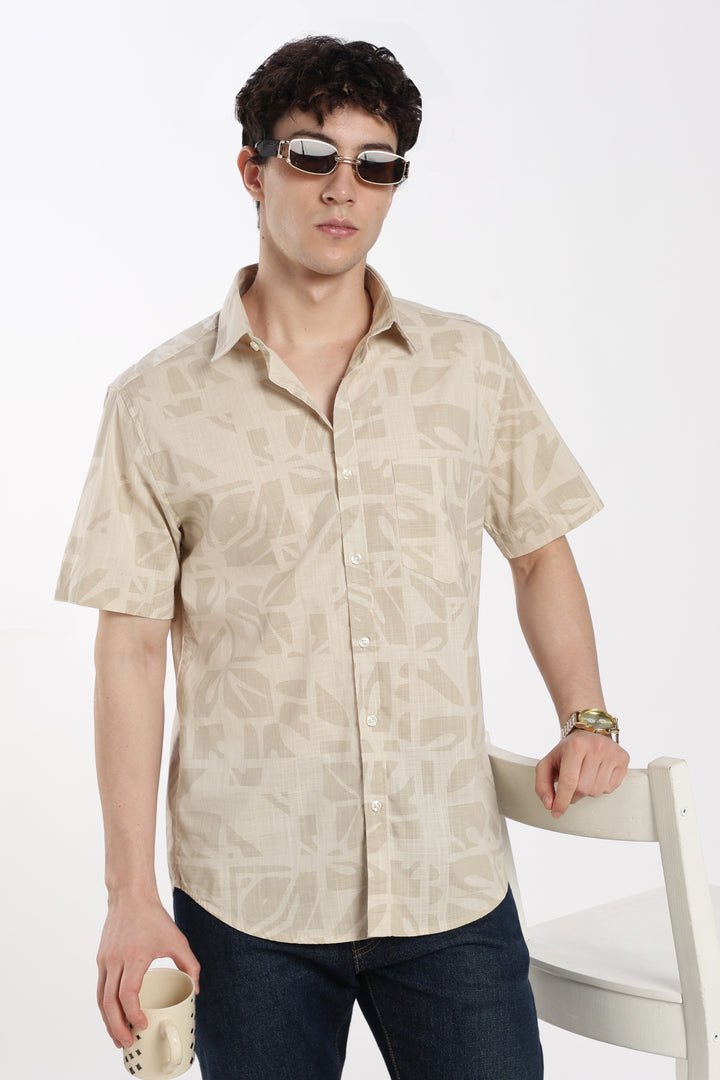 Man wearing a beige patterned half sleeve shirt and sunglasses on a white background
