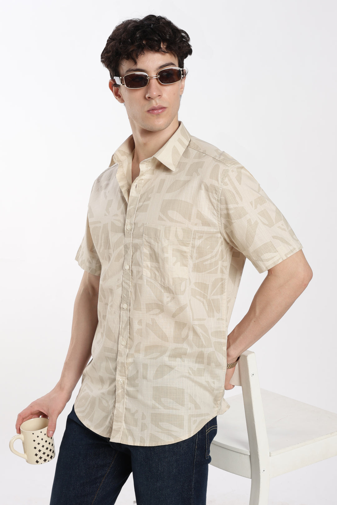Man wearing a beige patterned half sleeve shirt and sunglasses on a white background