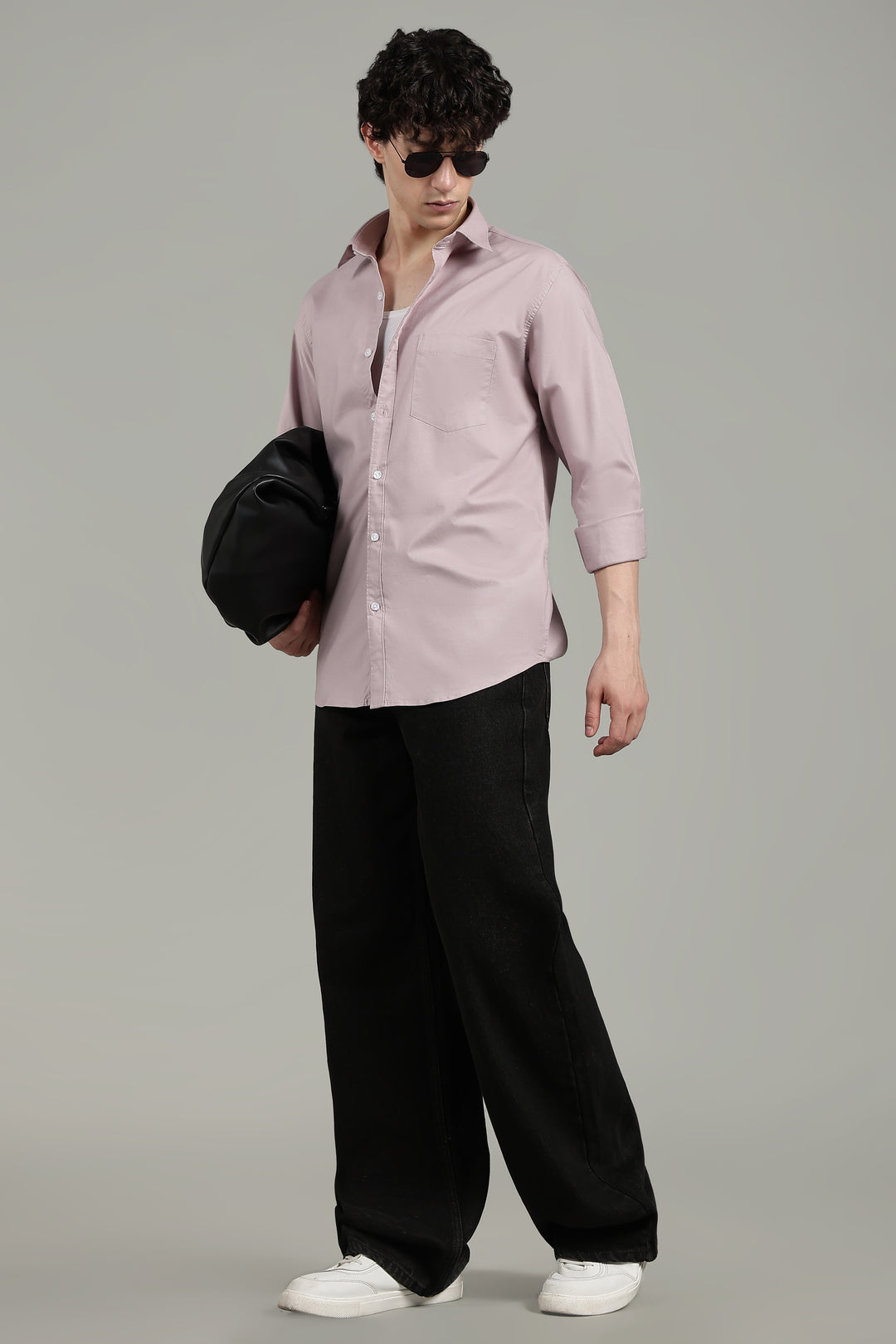 man  wearing a mute pink shirt and black pants, holding a black bag on a gray background