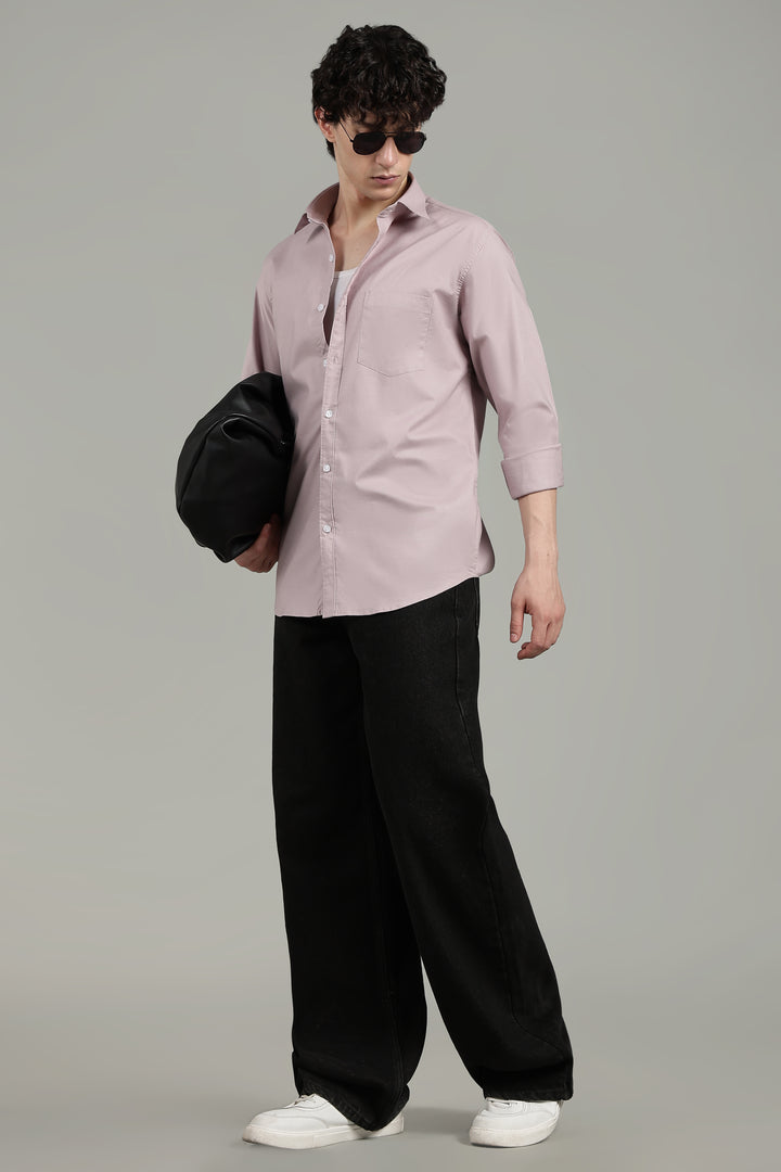 man  wearing a mute pink shirt and black pants, holding a black bag on a gray background